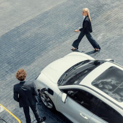 Aerial view progressive lifestyle of businesspeople with electric car connected to charging station at city center public parking car. Eco friendly rechargeable car powered by alternative clean energy