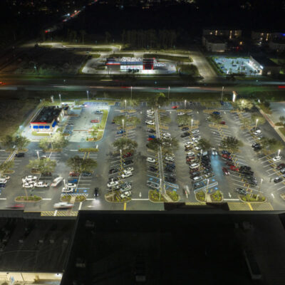 Aerial night view of many cars parked on parking lot with lines and markings for parking places and directions. Place for vehicles in front of a grocery mall store.